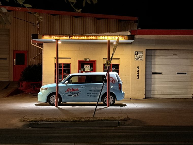 A mechanic's shop at night, as shot: a pale blue van under a lit sign reading Quality repairs by expert mechanics since 1990.