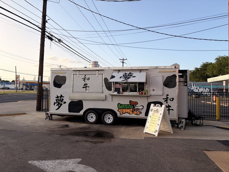 The food truck as shot: even daylight, blue sky, black markings on a white trailer.