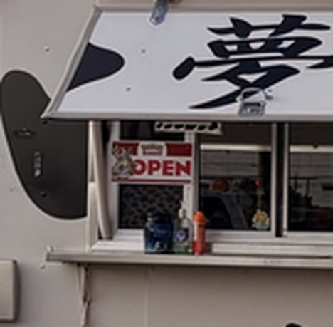 Close crop of the food truck window: a red and white sign clearly reading OPEN, under a large painted Japanese character.
